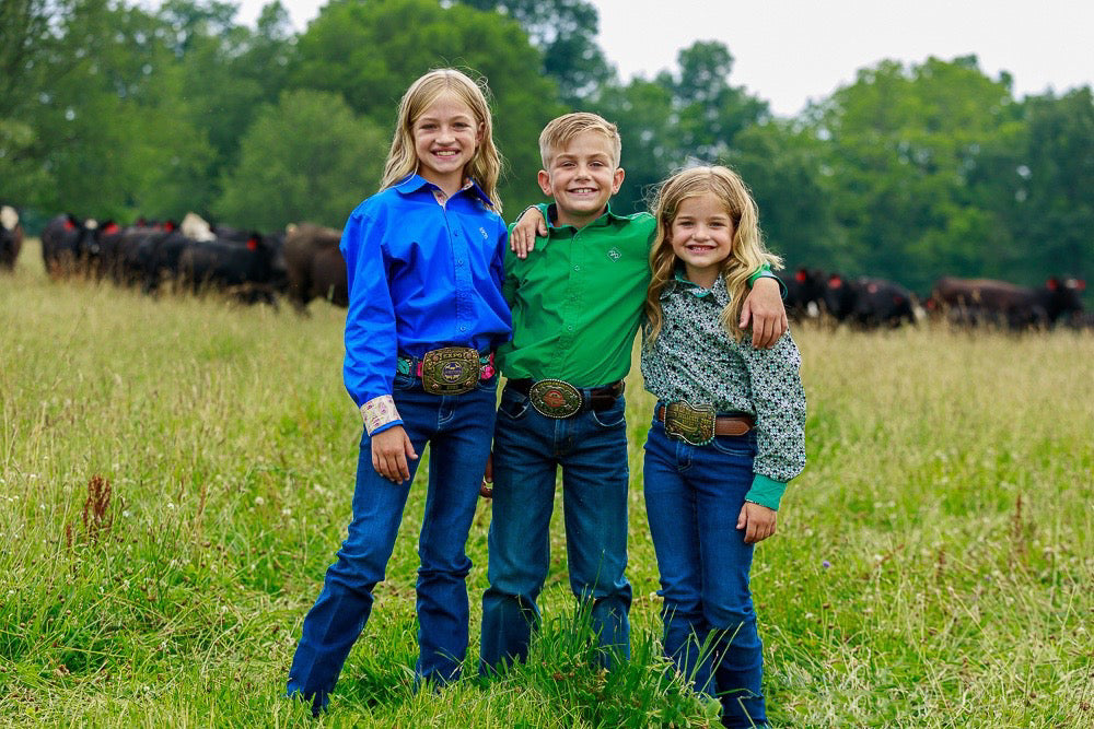 Kids in a hayfield with cattle in a blue, green and patterned show shirt and jeans.